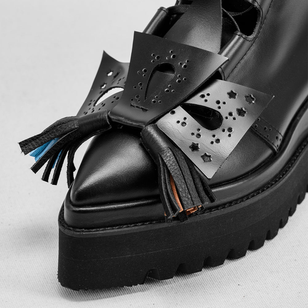 Black platform shoe with decorative bow and tassel on a light gray background
