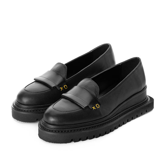 A pair of black leather flat shoes with a distinctive XO sewing detail on the top, featuring a natural leather lining and a black geometric sole.