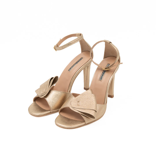 Moondust Gold leather sandals by Mihaela Glavan, three-quarter view showing the folded gold leather bows and ankle straps.