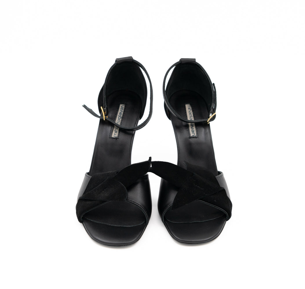 Front view of Our Time black leather sandals, with 3D black suede details and gold-tone ankle buckles.
