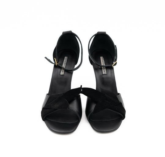 Front view of Our Time black leather sandals, with 3D black suede details and gold-tone ankle buckles.