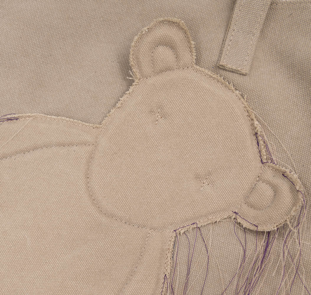 Close-up of the bear head applique, visible stitching and loose threads on the Teddy beige textile totebag.