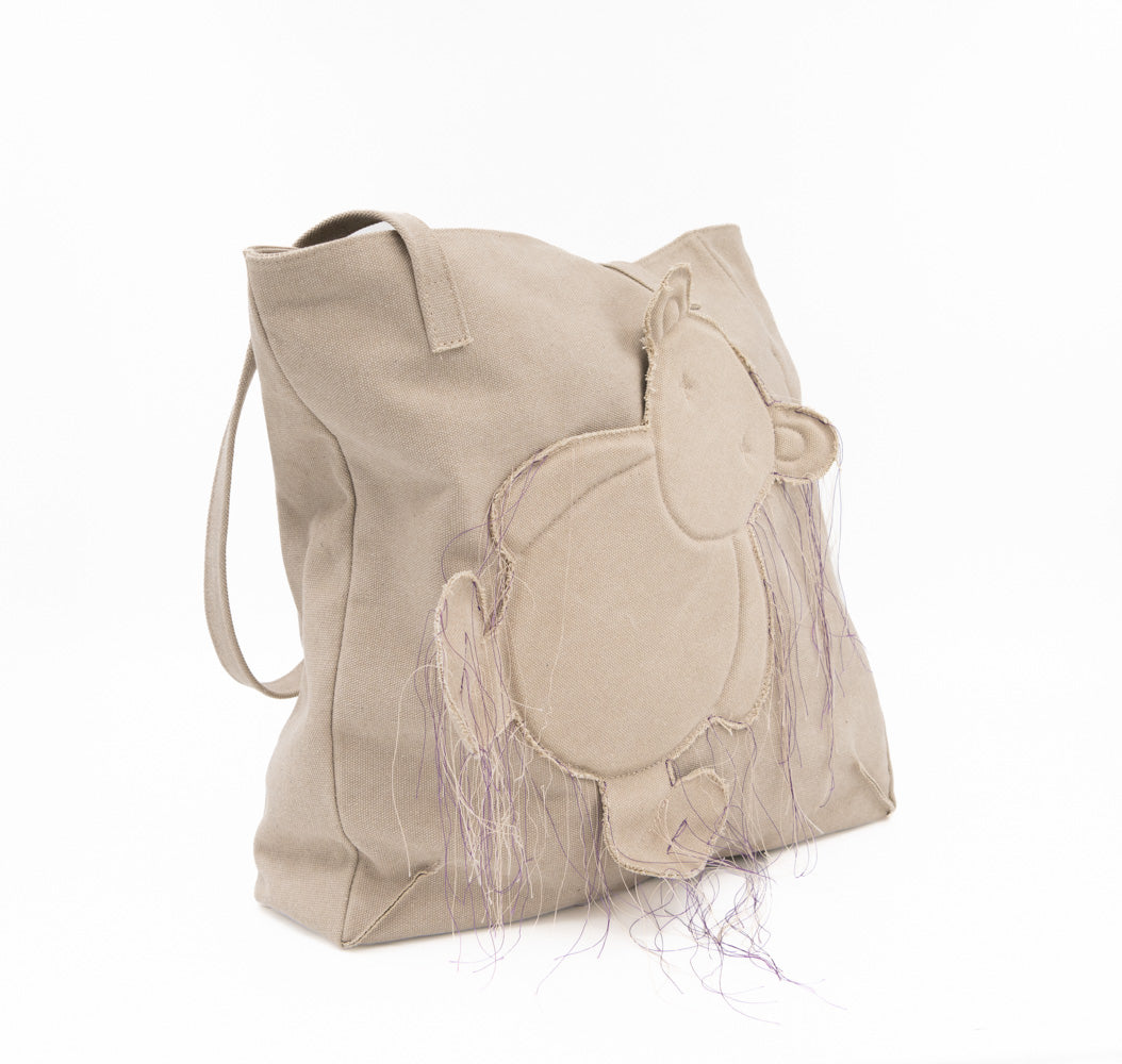 Teddy vegan beige textile totebag with a bear applique and long loose threads, three-quarter view.