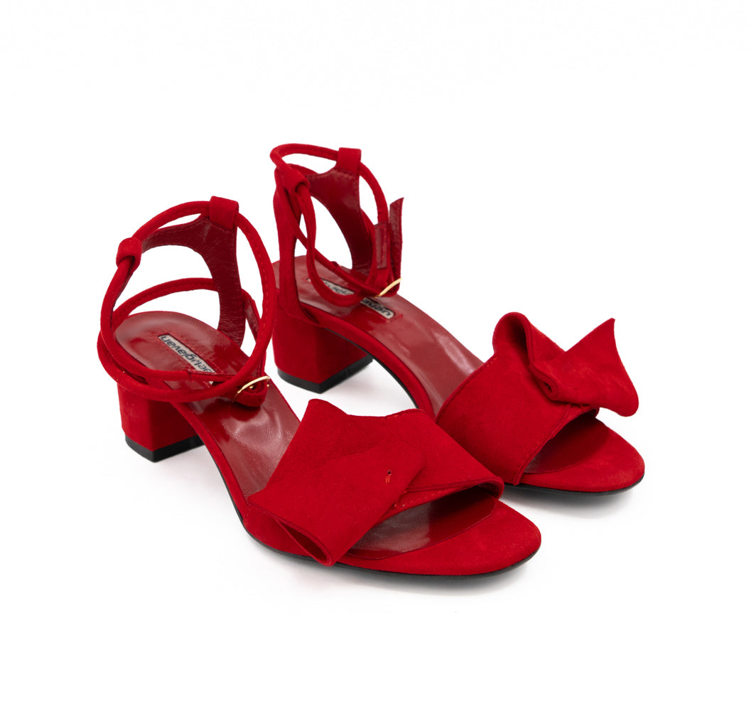 Angled view of Trick Me red suede sandals, highlighting the sculptural bows across the front.