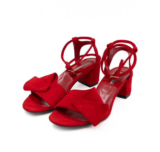 Trick Me red suede sandals by Mihaela Glavan, three-quarter front view with sculptural bows and ankle straps.