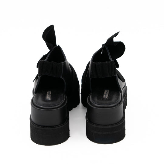 Rear view of Tulips black leather shoes, showing the open backs, elastic straps and black platform soles.